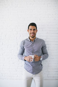 Young businessman standing against wall, holding cup up coffee