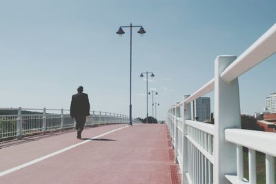 Rear view of man walking on bridge against clear sky