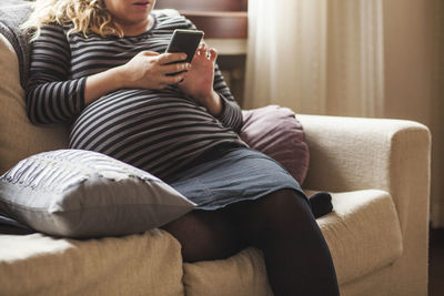 Midsection of man using mobile phone while sitting on sofa at home