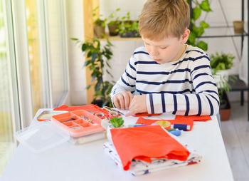 A caucasian boy of 9 years old is learning to sew with his hands homemade gift for mom for a holiday