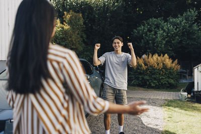 Cheerful young man holding fist while celebrating with mother in back yard
