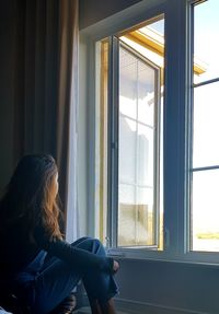 Woman looking through window at home