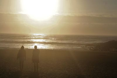 Rear view of couple standing on beach at sunset