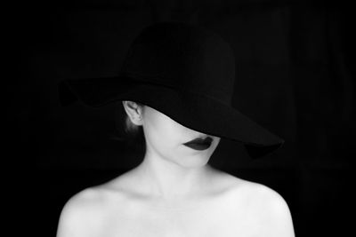 Shirtless woman wearing hat and lipstick against black background