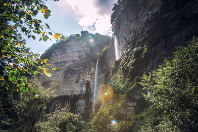 Low angle view of sunlight streaming through rocks against sky