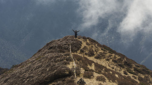 High angle view of man with arms outstretched standing on mountain peak