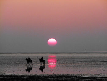 Men in sea against sky during sunset