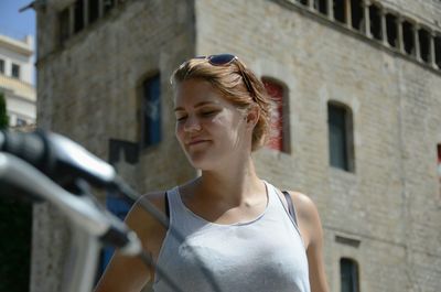 Young woman looking away while standing against built structure in city