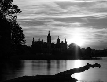 Silhouette of building by river against cloudy sky