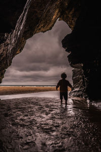 Man standing on rock at beach against sky