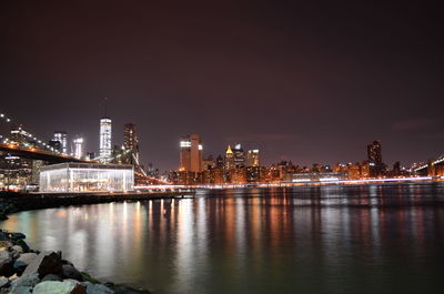 Illuminated buildings in city by river against sky at night