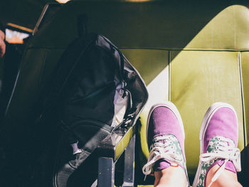 Low section of person in purple shoes by bag on vehicle seat