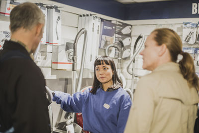 Young saleswoman explaining about appliances to mature customers in store