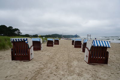 Hooded chairs on beach against sky