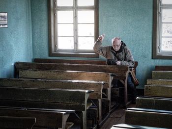 Man pointing while sitting on bench in classroom