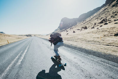 Rear view of man skateboarding on road against sky