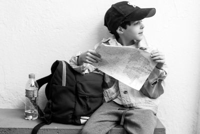 Boy holding map while sitting on table against wall