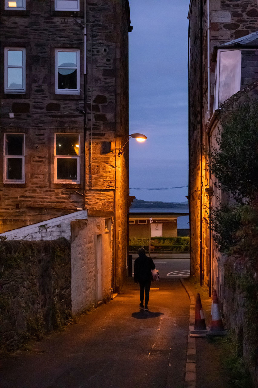 MAN WALKING ON ALLEY AMIDST BUILDINGS