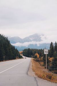 Road sign by trees against sky