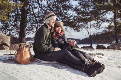 Happy couple enjoying coffee while relaxing on snow covered field