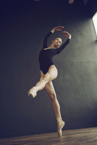 A ballerina in a bodysuit and pointe shoes moves around the room with long strides