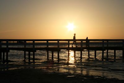 Silhouette pier over sea against sky during sunset