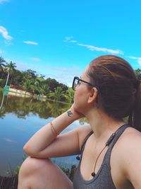 Portrait of young woman looking away while sitting by plants against sky