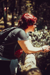 Side view of woman with redhead standing by railing in forest