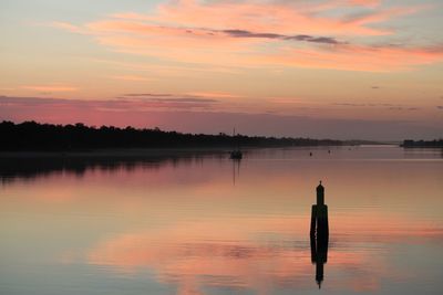 Silhouette wooden posts in lake against sky during sunset