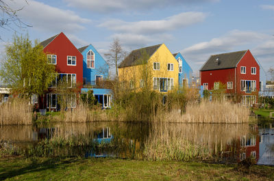 Scandinavian style houses with wooden facades in primary colors reflect in a pond in the golden hour