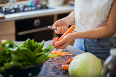 Midsection of woman peeling carrot in kitchen