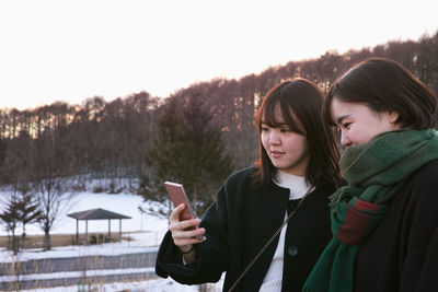 Young woman using phone while standing on snow