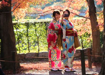 Happy young woman standing against trees during autumn