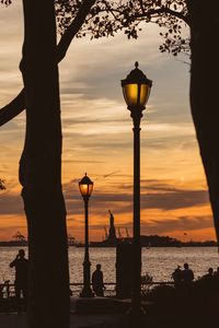 Silhouette of street light by sea during sunset