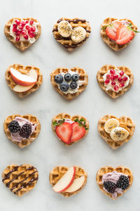 Several mini heart shaped waffles with various toppings.