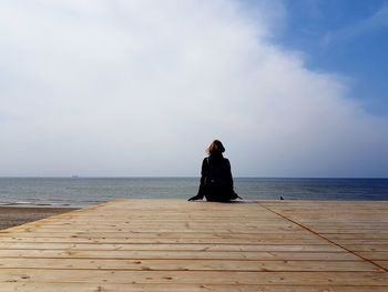 Rear view of woman sitting on beach against sky