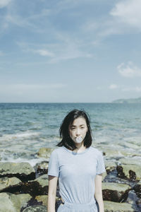 Portrait of young woman blowing bubble gum at beach against sky