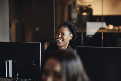 Happy businesswoman with computer looking away while sitting in office