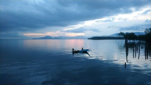 Silhouette man in sea against sky during sunset