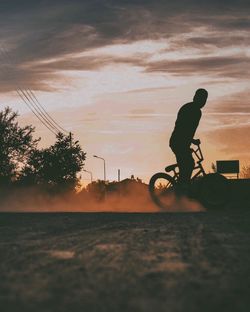 Silhouette man riding bicycle against sky during sunset