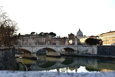 Arch bridge over river by buildings against clear sky