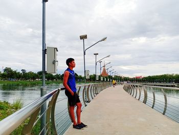 Man standing on railing against sky