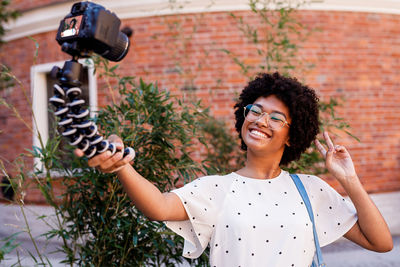 Smiling girl taking selfie through monopod against brick wall