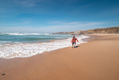 Rear view of woman walking at beach against sky