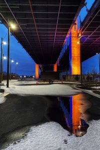Illuminated bridge over road against sky in city at night