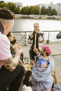 Happy non-binary person having pizza with friends near promenade in city