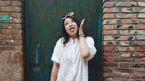 Portrait of smiling young woman standing against brick wall