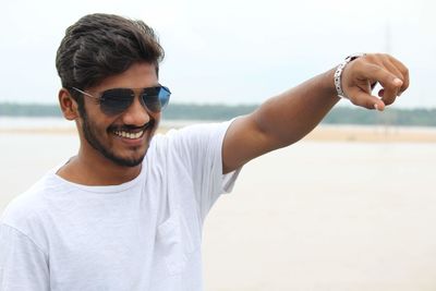 Portrait of young man wearing sunglasses while standing at beach