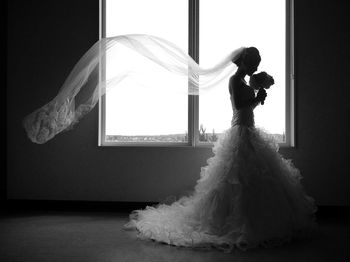 Bride in dress standing by window at home