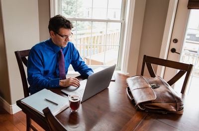 Man in shirt and tie working from home using computer at dining table.